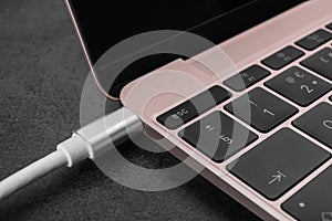 USB cable plugged into laptop port on dark table, closeup