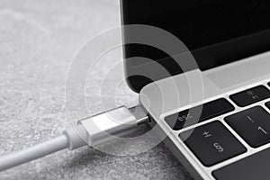 USB cable with type C connector plugged into laptop port on grey table
