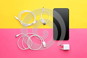 USB charge cables, power adapter and smartphone on color background. Modern technology