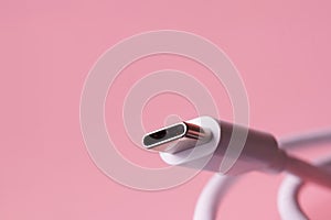 USB Type-C connector with a white wire on a pink background. Selective focus. Macro photo