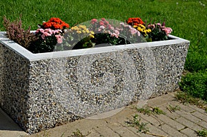 Use of annuals plants in concrete and brown plastic boxes near benches, polycarbonate bus stop. concrete parking for bicycles