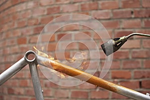 Use of a blowtorch to remove the paint of an orange bicycle frame