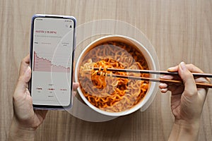 Use chopsticks eating noodles while using mobile phone monitor investment on stock, crypto trading