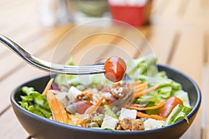 Use a fork a tomato skewer in the foreground and a salad in the background. Breakfast salad with sauteed vegetables on a wooden