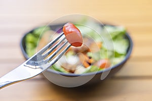 Use a fork a tomato skewer in the foreground and a salad in the background. Breakfast salad with sauteed vegetables on a wooden