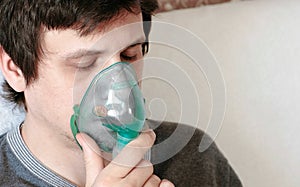 Use nebulizer and inhaler for the treatment. Closeup young man`s face with cloused eyes inhaling through inhaler mask