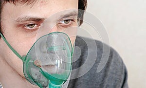 Use nebulizer and inhaler for the treatment. Closeup young man`s face inhaling through inhaler mask. Front view.