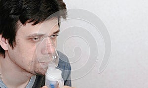 Use nebulizer and inhaler for the treatment. Closeup young man`s face inhaling through inhaler mask. Side view.