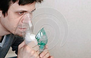 Use nebulizer and inhaler for the treatment. Closeup young man`s face inhaling through inhaler mask. Side view