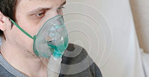 Use nebulizer and inhaler for the treatment. Closeup young man`s face inhaling through inhaler mask. Side view.