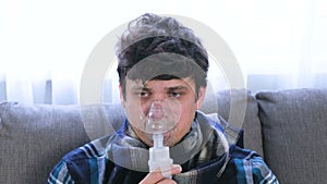 Use nebulizer and inhaler for the treatment. Sick man inhaling through inhaler mask sitting on the sofa. Close-up face.