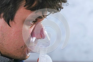 Use nebulizer and inhaler for the treatment. Sick man inhaling through inhaler mask sitting on the sofa. Close-up face