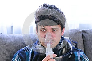 Use nebulizer and inhaler for the treatment. Sick man inhaling through inhaler mask sitting on the sofa. Close-up face.