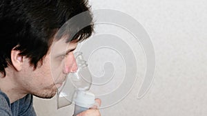 Use nebulizer and inhaler for the treatment. Young man inhaling through inhaler mask and coughs. Side view.