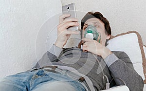 Use nebulizer and inhaler for the treatment. Young man inhaling through inhaler mask lying on the couch and chatting in