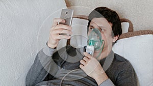 Use nebulizer and inhaler for the treatment. Young man inhaling through inhaler mask lying on the couch and chatting in