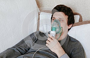 Use nebulizer and inhaler for the treatment. Young man inhaling through inhaler mask lying on the couch. Side view.