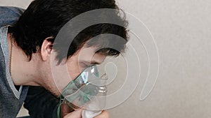 Use nebulizer and inhaler for the treatment. Young man inhaling through inhaler mask. Side view.