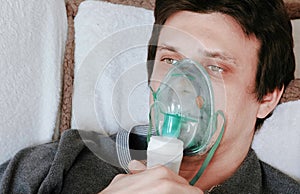 Use nebulizer and inhaler for the treatment. Young man`s face inhaling through inhaler mask lying on the couch. Side