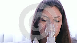 Use nebulizer and inhaler for the treatment. Young woman inhaling through inhaler mask. Close-up face, front view.