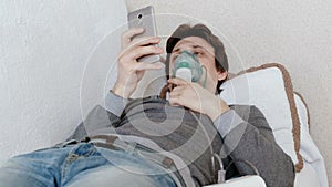 Use nebulizer and inhaler for the treatment. Young woman inhaling through inhaler mask lying on the couch and chatting