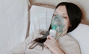 Use nebulizer and inhaler for the treatment. Young woman inhaling through inhaler mask lying on the couch. Closeup front