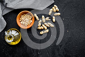 Use nut oil as cosmetics. Peanut oil in jar near peanut in bowl on black background top view copy space