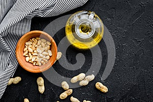 Use nut oil as cosmetics. Peanut oil in jar near peanut in bowl on black background top view copy space