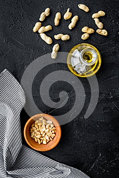 Use nut oil as cosmetics. Peanut oil in jar near peanut in bowl on black background top view copy space