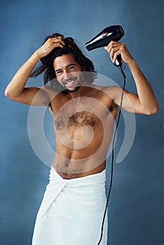 Use proper care to maintain great hair. Studio portrait of a handsome young man blowdrying his hair against a blue