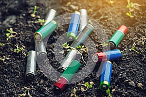 Used alkaline batteries lie in the soil where plants grow. Concept of environmental pollution with toxic household waste
