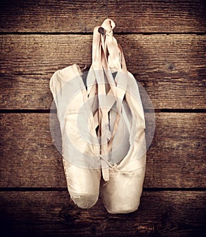 Used ballet shoes hanging on wooden background