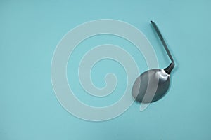 A used and bent spoon, isolated on a blue background.