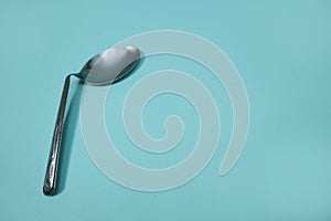 A used and bent spoon, isolated on a blue background.