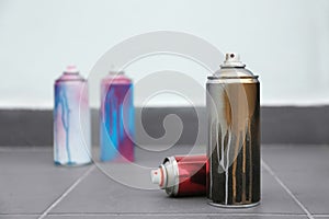 Used cans of spray paint on floor indoors.