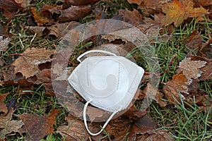 A used but clean medical respirator lies on the ground in the grass and autumn leaves in the hoarfrost.