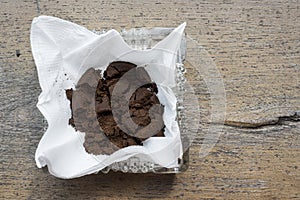 Used coffee grounds in white paper tissue in square glass ashtray on wooden board