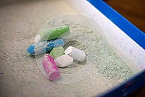 Used colored chalks with chalk powder dust in a box.