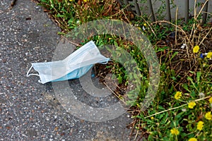 Used and contaminated face mask discarded as waste on the side of the road, not collected, not recyclable, and not biodegradable