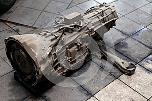 The used gearbox removed from the car on the floor among other parts in the vehicle repair workshop. Spare parts for transport in