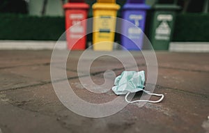 Used medical face mask discard on pavement floor on blurred recycle bin or trash. Medical waste disposal with unhygienic.