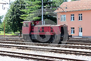 Used old dark red electric locomotive waiting for departure in front of new railway station building