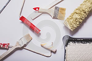 Used painting tools with red handles covered in warm white paint layed out in a composition on a plain white background