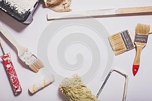 Used painting tools with red handles covered in warm white paint layed out in a composition on a plain white background