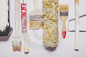 Used painting tools with red handles covered in warm white paint