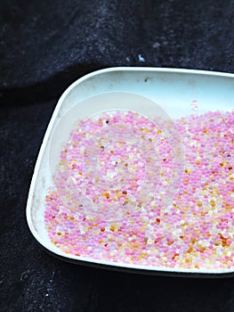 Used pink coloured blue silica gel from a camera lens keeping box in plastic dish on house roof in sun drying process