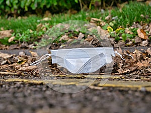 A used, surgical face mask used for COVID-19 PPE protection, discarded as litter on a pavement / sidewalk
