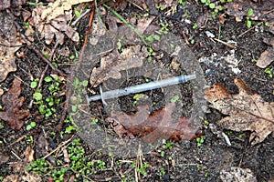 Used syringe on the ground among autumn leaves