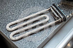 Used washing machine heating element covered with limescale placed on gray countertop surface