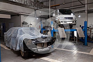 Used white van car raised on a blue  lift for repairing the chassis and engine in a vehicle repair workshop. Auto service industry